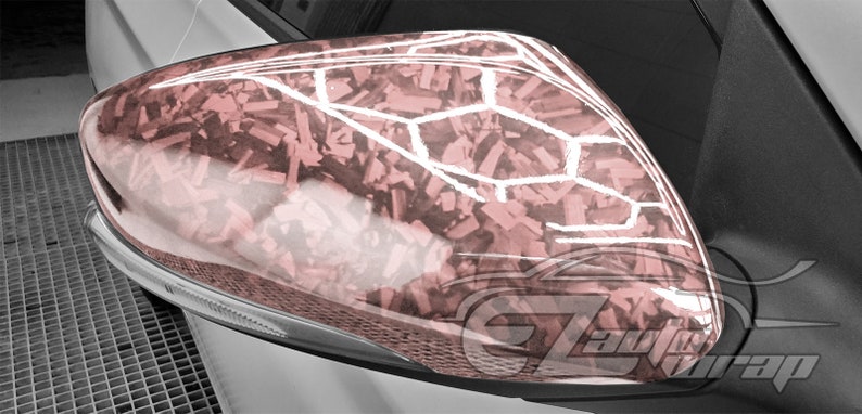 May include: A close-up of a car's side mirror with a pink and white camouflage pattern. The mirror is made of plastic and has a glossy finish.