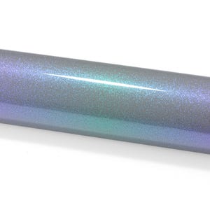 May include: A cylindrical roll of adhesive vinyl featuring a smooth, reflective surface with a color-shifting gradient effect that transitions from deep purple to vibrant teal and silver, covered in a fine, dense layer of sparkling glitter particles.