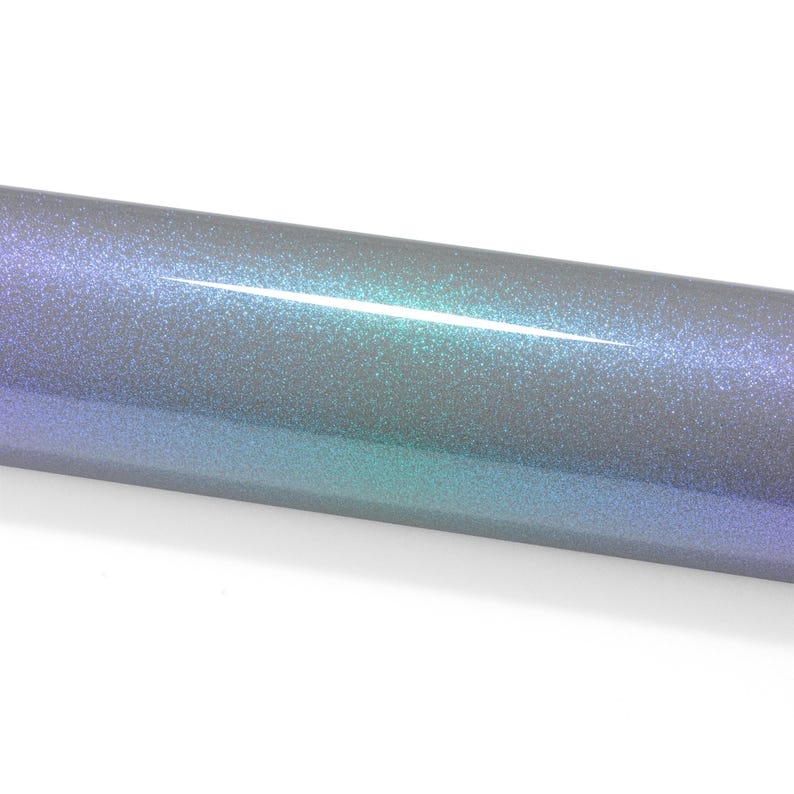 May include: A cylindrical roll of adhesive vinyl featuring a smooth, reflective surface with a color-shifting gradient effect that transitions from deep purple to vibrant teal and silver, covered in a fine, dense layer of sparkling glitter particles.