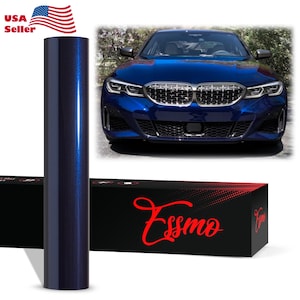 May include: A roll of dark blue metallic vinyl wrap film standing vertically next to a black rectangular box with the red text Essmo printed on it. A blue sedan is shown in the background to demonstrate the application of the vinyl wrap.