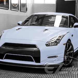 May include: A light blue sports car featuring a black front grille, sharp angular headlights, and dark multi-spoke wheels. The vehicle has a low-profile design with a prominent front bumper and a smooth, matte-finish exterior body paint.