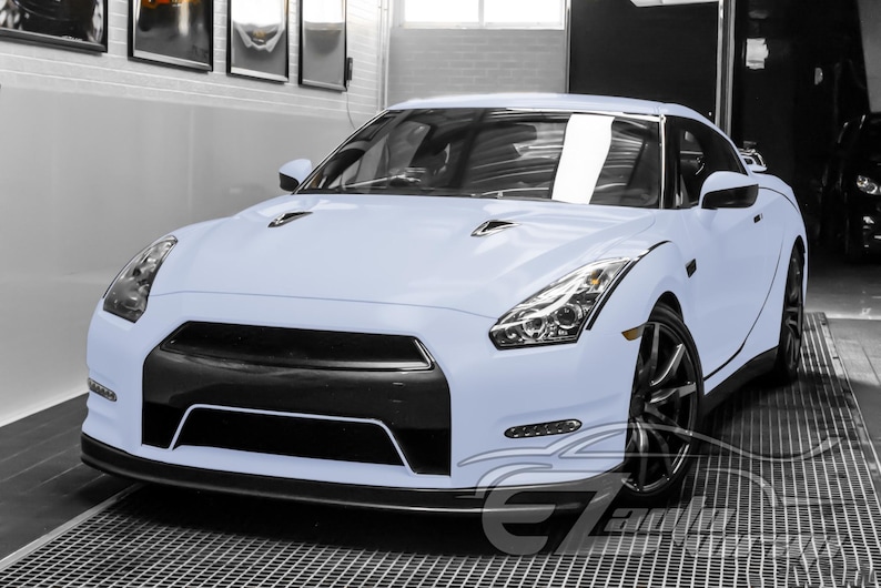 May include: A light blue sports car featuring a black front grille, sharp angular headlights, and dark multi-spoke wheels. The vehicle has a low-profile design with a prominent front bumper and a smooth, matte-finish exterior body paint.