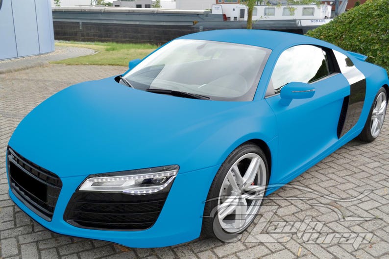 May include: A matte light blue sports car featuring a sleek aerodynamic body, silver alloy wheels, and black side air intake panels. The front end displays sharp LED headlights and a black grille. A watermark is visible in the bottom right corner.