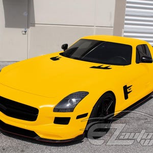 May include: A bright yellow sports car featuring a sleek aerodynamic body, black front grille, black side mirrors, and black multi-spoke wheels. The vehicle has tinted windows and black air vents on the hood. The text EZAutoWrap is visible.