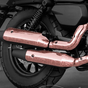 May include: A black motorcycle with rose gold exhaust pipes. The motorcycle has a black seat and a black tire with a tread pattern. The exhaust pipes are made of metal and have a shiny finish.