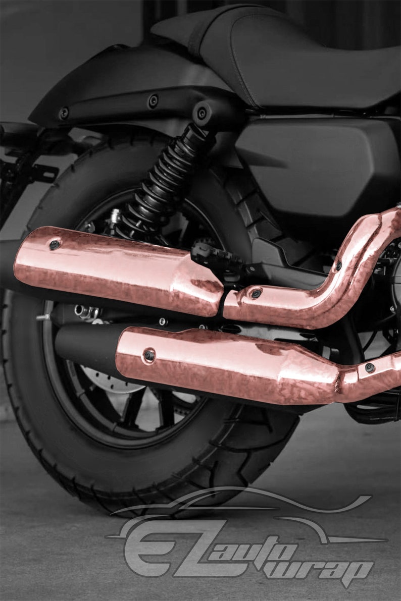 May include: A black motorcycle with rose gold exhaust pipes. The motorcycle has a black seat and a black tire with a tread pattern. The exhaust pipes are made of metal and have a shiny finish.