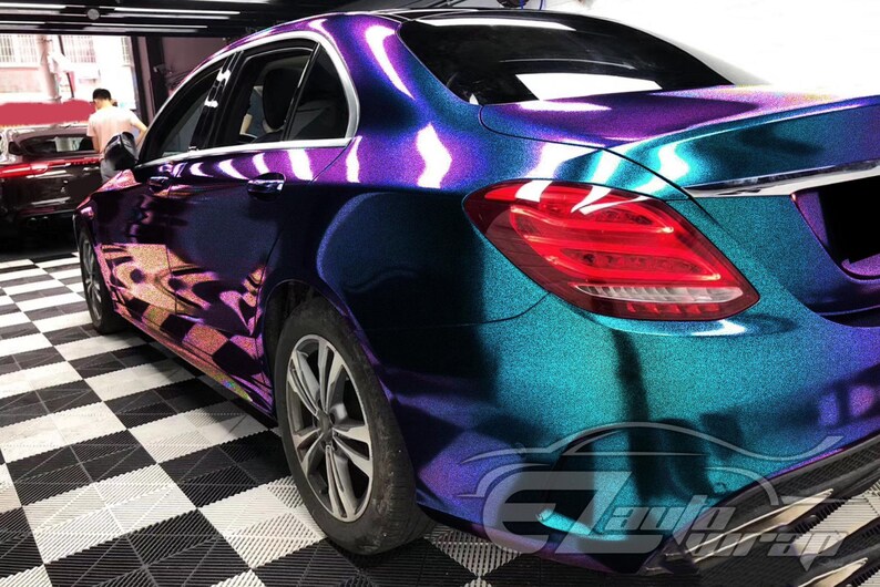 May include: A sedan featuring a color-shifting vinyl wrap that transitions between deep purple, blue, and teal hues with a metallic glitter finish. The vehicle has silver alloy wheels, red taillights, and chrome window trim accents.