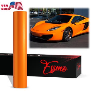 May include: A vertical roll of glossy orange vinyl wrap film positioned next to a black rectangular box featuring the brand name Essmo in red script. Above the box, a photograph displays a bright orange sports car parked in a lot.