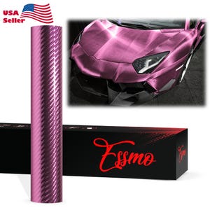 May include: A cylindrical roll of pink carbon fiber vinyl wrap featuring a textured weave pattern. The roll is positioned next to a black rectangular box with the red text Essmo printed on the front, and a car wrapped in the same material.