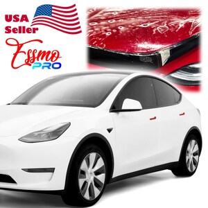 May include: White Tesla Model Y with black trim and red door handles. The car is shown with a clear protective film on the hood, which has several small scratches and marks.