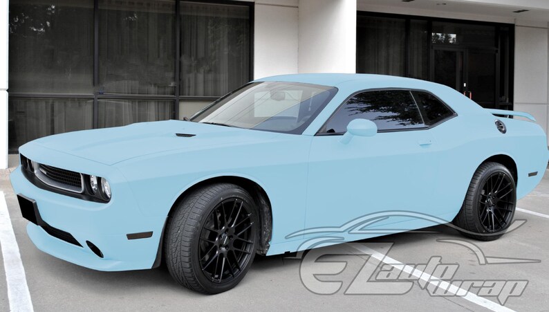 May include: A light blue two-door coupe car featuring a matte finish, black multi-spoke alloy wheels, tinted windows, and a rear spoiler. The vehicle has a low-profile stance with a prominent front grille and a watermark logo in the bottom right corner.