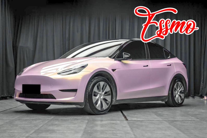 May include: A pink Tesla Model Y with black accents and tinted windows. The car is parked in a studio setting with a black backdrop.