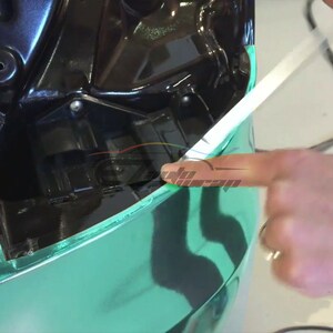 May include: A close-up of a car being wrapped in a teal green vinyl wrap. A person's hand is holding a squeegee to smooth out the vinyl.