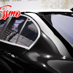May include: A black car exterior featuring a carbon fiber pattern wrap on the rear pillar and door panel. The vehicle has a white roof section, silver window trim, and a black shark fin antenna. The red text Essmo is visible in the upper left corner.