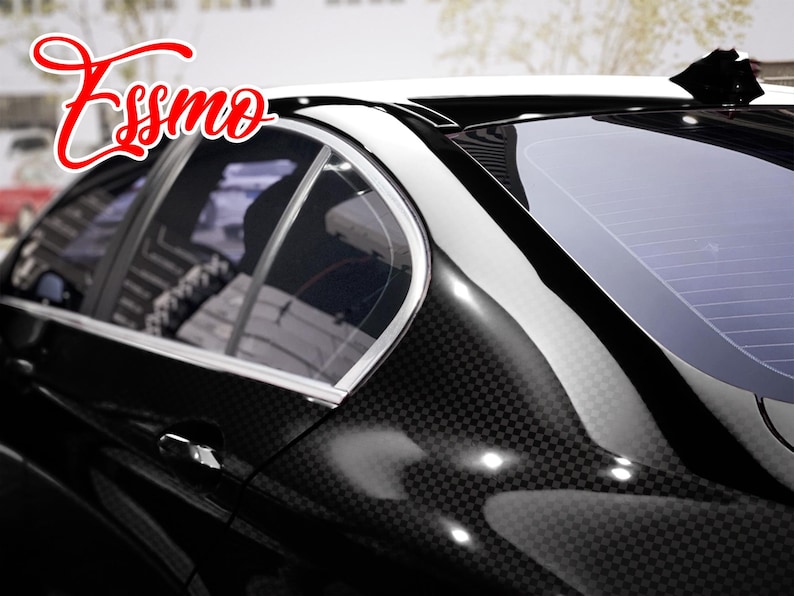 May include: A black car exterior featuring a carbon fiber pattern wrap on the rear pillar and door panel. The vehicle has a white roof section, silver window trim, and a black shark fin antenna. The red text Essmo is visible in the upper left corner.