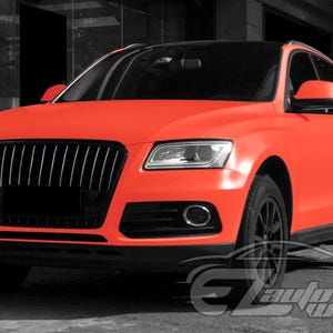May include: A bright neon orange SUV featuring a matte finish, a black front grille, black side mirrors, and black wheels. The vehicle has a sleek design with clear headlights and a black roof, showcasing a bold and vibrant exterior color scheme.