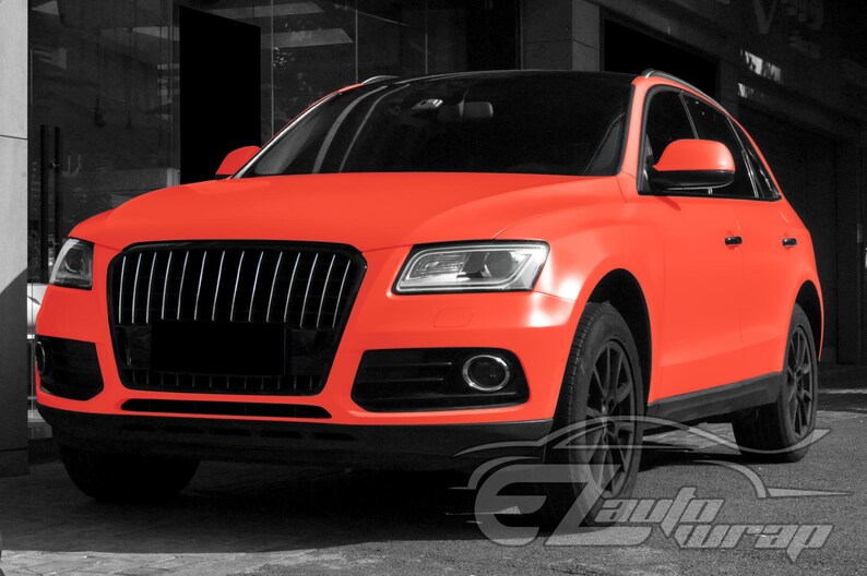 May include: A bright neon orange SUV featuring a matte finish, a black front grille, black side mirrors, and black wheels. The vehicle has a sleek design with clear headlights and a black roof, showcasing a bold and vibrant exterior color scheme.