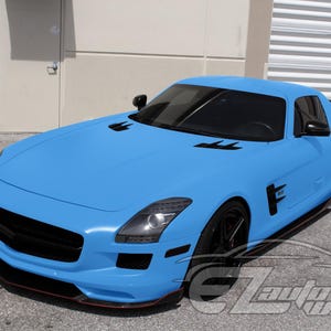 May include: A matte light blue sports car with a long hood, black wheels, black side mirrors, and black air vents on the hood and side panels. The vehicle features tinted windows and a black front grille. The text EZAutoWrap is visible in the corner.