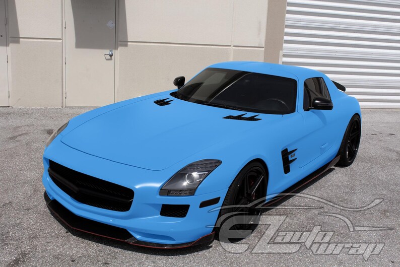 May include: A matte light blue sports car with a long hood, black wheels, black side mirrors, and black air vents on the hood and side panels. The vehicle features tinted windows and a black front grille. The text EZAutoWrap is visible in the corner.
