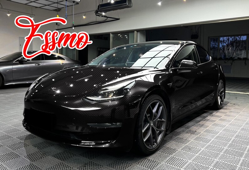 May include: A black sedan with a visible carbon fiber weave pattern on the exterior body panels. The vehicle features dark grey multi-spoke alloy wheels and sleek headlights. The word Essmo is written in a red cursive font in the upper left corner.