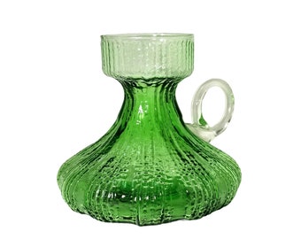 May include: A green glass pitcher with a textured surface and a clear handle. The pitcher has a bulbous base and a cylindrical top. The handle is small and rounded. The pitcher is likely used for serving beverages.