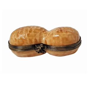 May include: A decorative peanut-shaped trinket box. The box is light brown with a textured surface, resembling a peanut shell. It features a hinged design with a dark metal band and clasp, adding a touch of elegance to the novelty item.