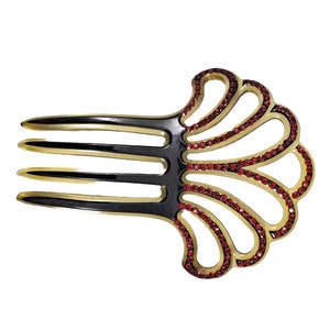 May include: A black and gold hair comb with a decorative shell design. The shell is outlined with red rhinestones.