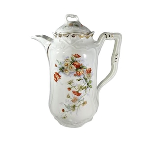 May include: White porcelain coffee pot with a lid, featuring a floral design in shades of red, orange, and cream. The pot has a curved handle and a spout. Gold trim accents the lid and the top of the pot.