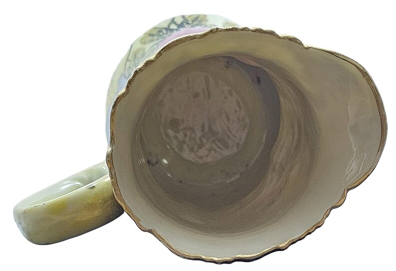 Może przedstawiać: Wazon ceramiczny w stylu vintage z falistym brzegiem i uchwytem. Wazon ma kremowe wnętrze i jasnozielony wygląd zewnętrzny ze złotym wykończeniem. Na zewnątrz widoczne są kwiatowe wzory.