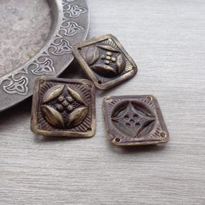 Könnte beinhalten: Drei antike Messing-Dekorverzierungen mit filigranen Blumendesigns. Die Verzierungen sind quadratisch mit abgerundeten Ecken und haben eine dunkelbraune Patina.