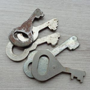 May include: A collection of vintage metal keys with a worn, aged appearance. The keys have a simple, functional design with a circular opening and a keyhole-shaped head. The metal shows signs of rust and wear, suggesting they are antique or reclaimed.