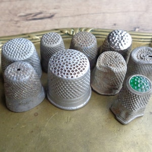 Può includere: Una collezione di nove ditale d'argento con vari motivi e disegni. Alcuni ditale hanno una superficie liscia, mentre altri hanno un design testurizzato o in rilievo. Un ditale ha una parte superiore in vetro verde.