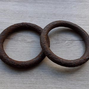 May include: Two circular metal rings with a heavily oxidized, dark brown, and textured surface. The rings are solid, thick, and display a weathered appearance with visible pitting and uneven corrosion across the entire circumference of each piece.