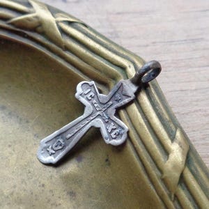 Può includere: Un ciondolo a forma di croce argentato con un'iscrizione in scrittura cirillica. Il ciondolo è su una superficie in ottone con un design decorativo.