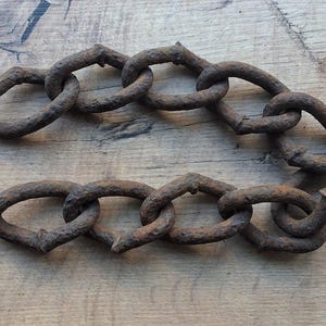 Puede incluir: Una cadena de metal resistente que presenta una serie de eslabones ovalados interconectados con un acabado marrón oscuro, desgastado y oxidado. La cadena está dispuesta en una formación curva en forma de U, mostrando una textura rugosa y oxidada.