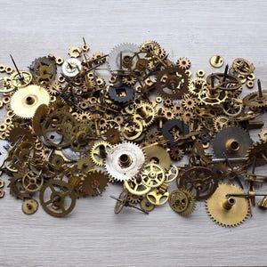 Op de afbeelding: Een verzameling diverse messing en zilverkleurige uurwerktandwielen en -onderdelen, verspreid op een licht houten oppervlak. De tandwielen variëren in grootte en ontwerp, met ingewikkelde details en texturen, ideaal voor steampunk of knutselprojecten.