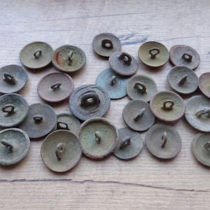 Puede incluir: Una colección de 20 botones de metal antiguos con una variedad de diseños. La mayoría de los botones son circulares con un borde elevado y un pequeño agujero en el centro. Algunos botones tienen un diseño decorativo en la parte delantera, mientras que otros son lisos. Los botones están todos en varios tonos de marrón, verde y gris.