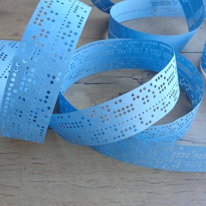 Peut inclure: Une longue bande de papier bleu clair en continu, présentant une série de trous perforés avec précision selon des motifs spécifiques. La bande de papier est enroulée en plusieurs boucles superposées, révélant une grille complexe de perforations.