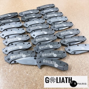 May include: A group of 18 gray pocket knives with the words "Goliath T Pars" engraved on each blade.