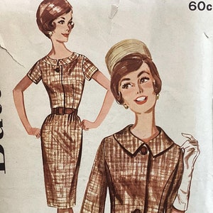 May include: Vintage sewing pattern featuring illustrations of a woman in a brown and tan plaid dress and jacket ensemble. The dress has a fitted silhouette with a belt, and the jacket is cropped. The pattern includes size options.