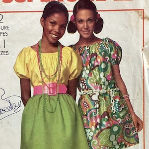 May include: Two young women in vintage dresses. One wears a yellow top, green skirt, and pink belt. The other wears a colorful patterned dress. The image is from a vintage sewing pattern.