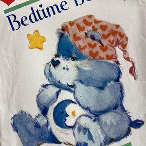 May include: A vintage sewing pattern envelope featuring Bedtime Bear from Care Bears. The blue bear wears a pink nightcap with red hearts and has a moon and star symbol on its belly. A yellow star is nearby. Text includes Bedtime Bear and 6226.
