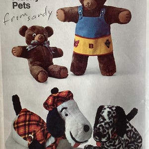 May include: A set of four plush toys including two brown bears and two dogs. One bear wears a blue and yellow apron with a letter B, the other a plaid bow. One dog wears a red plaid hat and cape, while the other has a black and white spotted pattern.