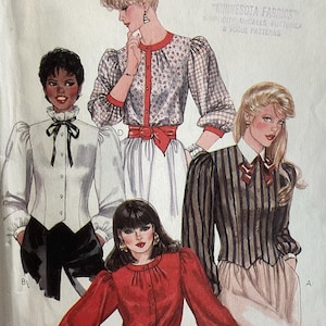 May include: A McCall's sewing pattern envelope featuring illustrations of four different blouse styles. The designs include long-sleeved tops with various necklines, button-front closures, and waist details, labeled with letters A, B, C, and D.