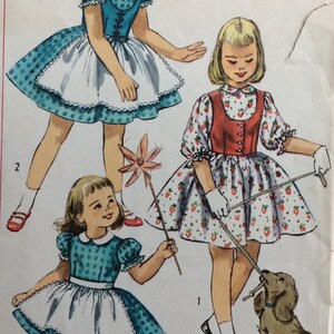 May include: A vintage illustration of three girls wearing dresses. The girl on the left is wearing a blue and white polka dot dress with a white apron. The girl in the middle is wearing a red and white dress with a strawberry pattern. The girl on the right is wearing a white dress with a red and white strawberry pattern. The girls are holding various items, including a pinwheel and a leash. A brown and white dog is sitting on the ground.