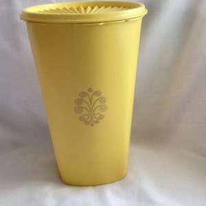 May include: A yellow plastic container with a lid. The container has a decorative floral design on the front. The lid has a ridged design. The container is approximately 10 inches tall.