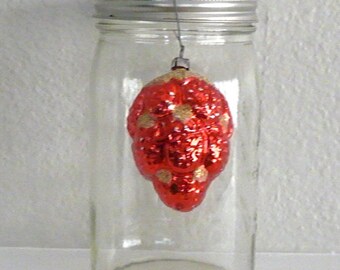 May include: A clear glass jar with a silver lid containing a red and gold Christmas bauble.