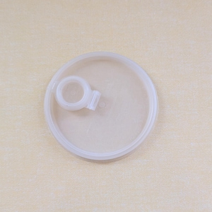 May include: A circular, semi-translucent white plastic lid featuring a raised, integrated ring-shaped pull tab positioned off-center on its flat surface. The lid has a smooth, slightly recessed interior area and a raised outer rim for sealing.