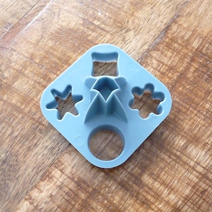 Puede incluir: Un cortador de galletas de plástico azul con cuatro formas diferentes: una estrella, una flor, un círculo y un cuadrado.