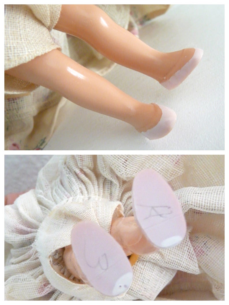 Puede incluir: Una mu&ntilde;eca vintage con un vestido blanco y zapatos rosas. Las piernas de la mu&ntilde;eca est&aacute;n dobladas en las rodillas y los zapatos son visibles. La mu&ntilde;eca lleva un vestido blanco con un estampado floral.